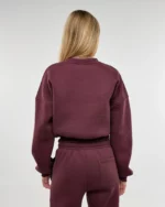 Mergina vilki burgundiškos spalvos sweatshirt džemperį ir stovi atsukusi nugarą