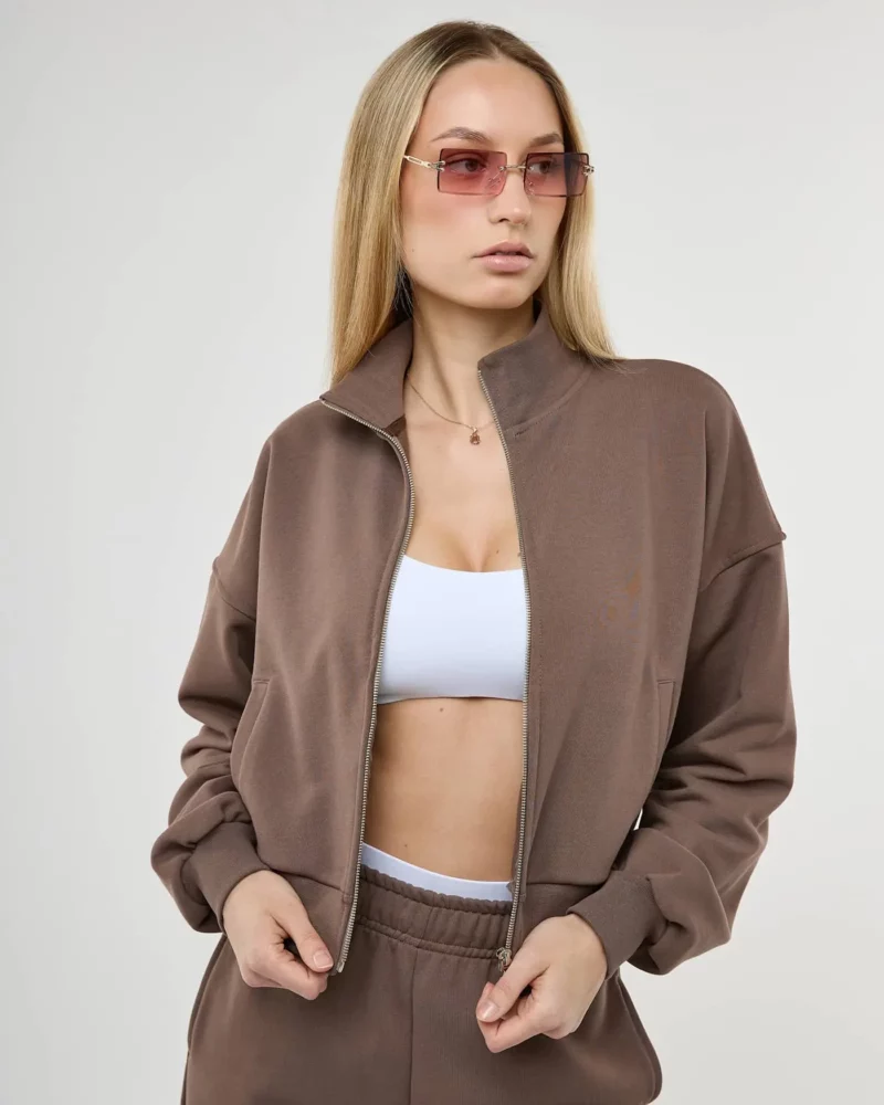 Šviesiaplaukė mergina dėvi rudą džemperį su užtrauktuku