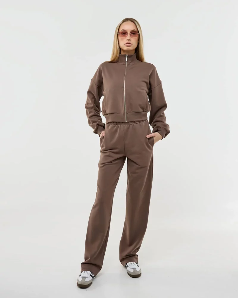 Šviesiaplaukė mergina dėvi rudą laisvalaikio kostiumėlį su užtrauktuku