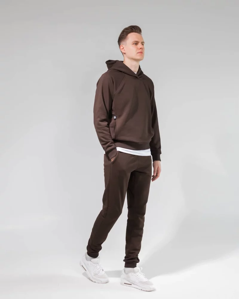 Vyras vilki tamsiai rudą laisvalaikio kostiumą - džemperį su kapišonu ir kelnes.